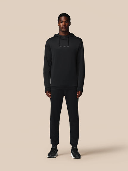 Person wearing a black hoodie and pants on a beige background