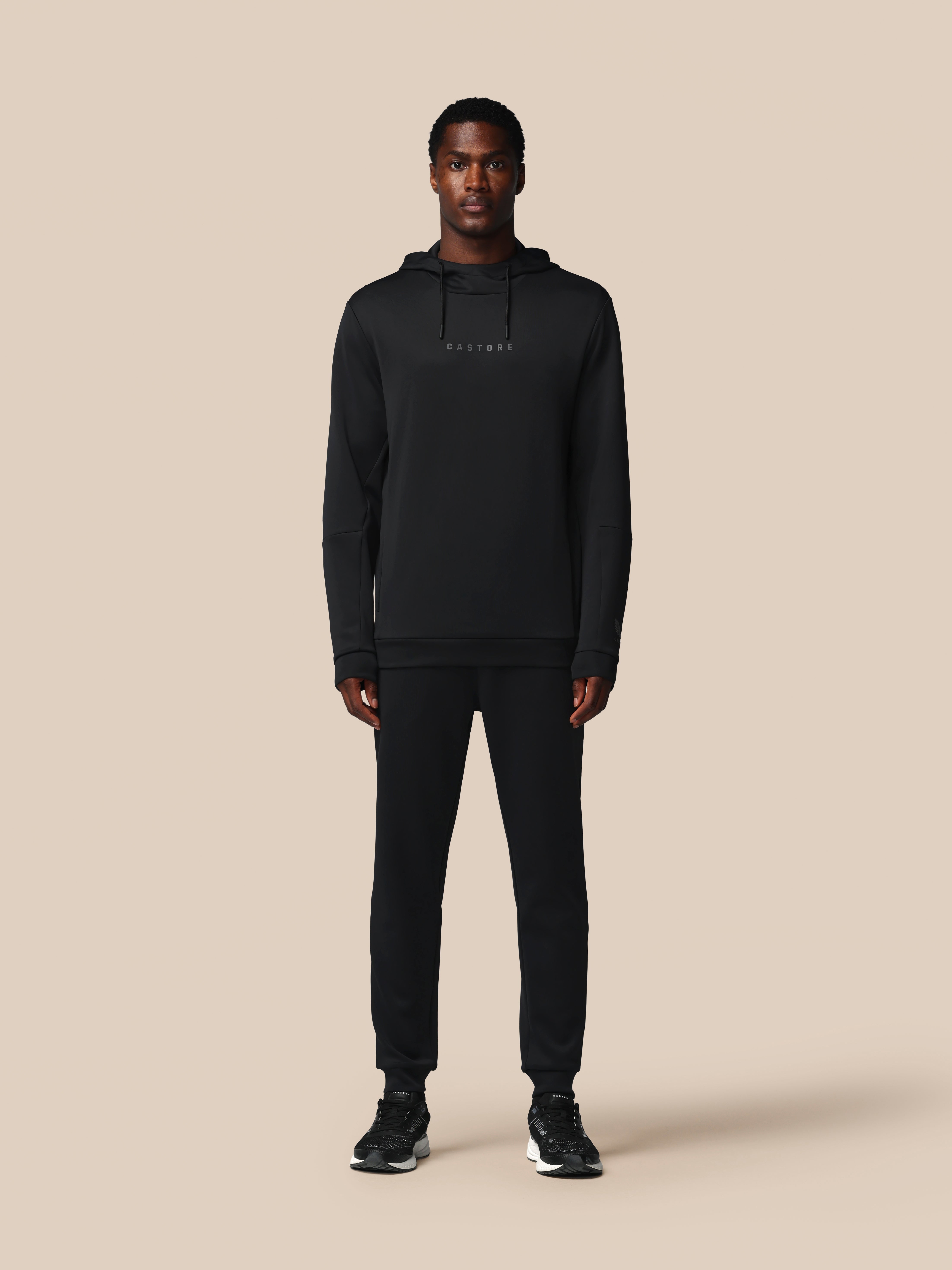 Person wearing a black hoodie and pants on a beige background