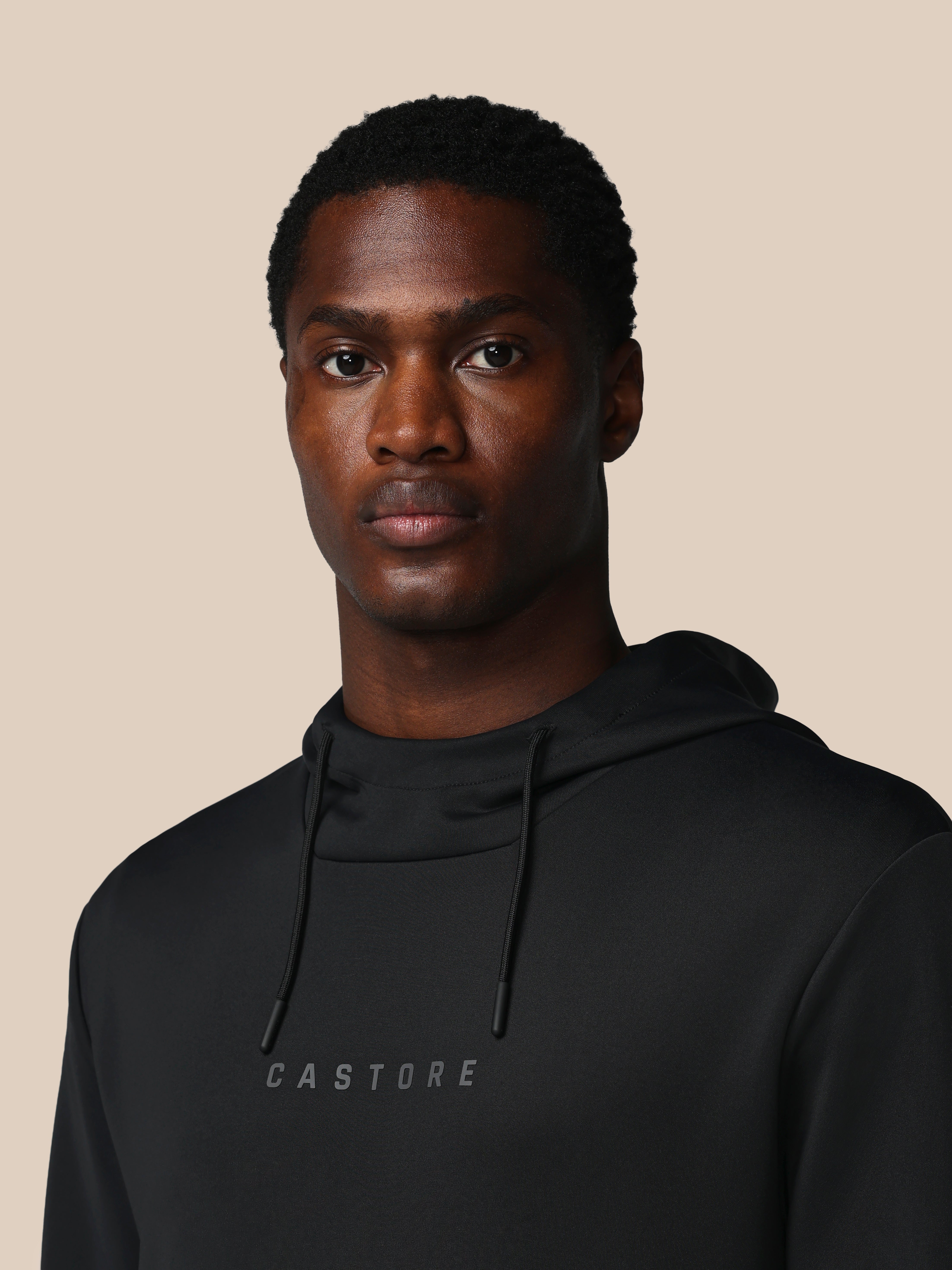 Man wearing a black hoodie with 'CASTORE' branding on a beige background