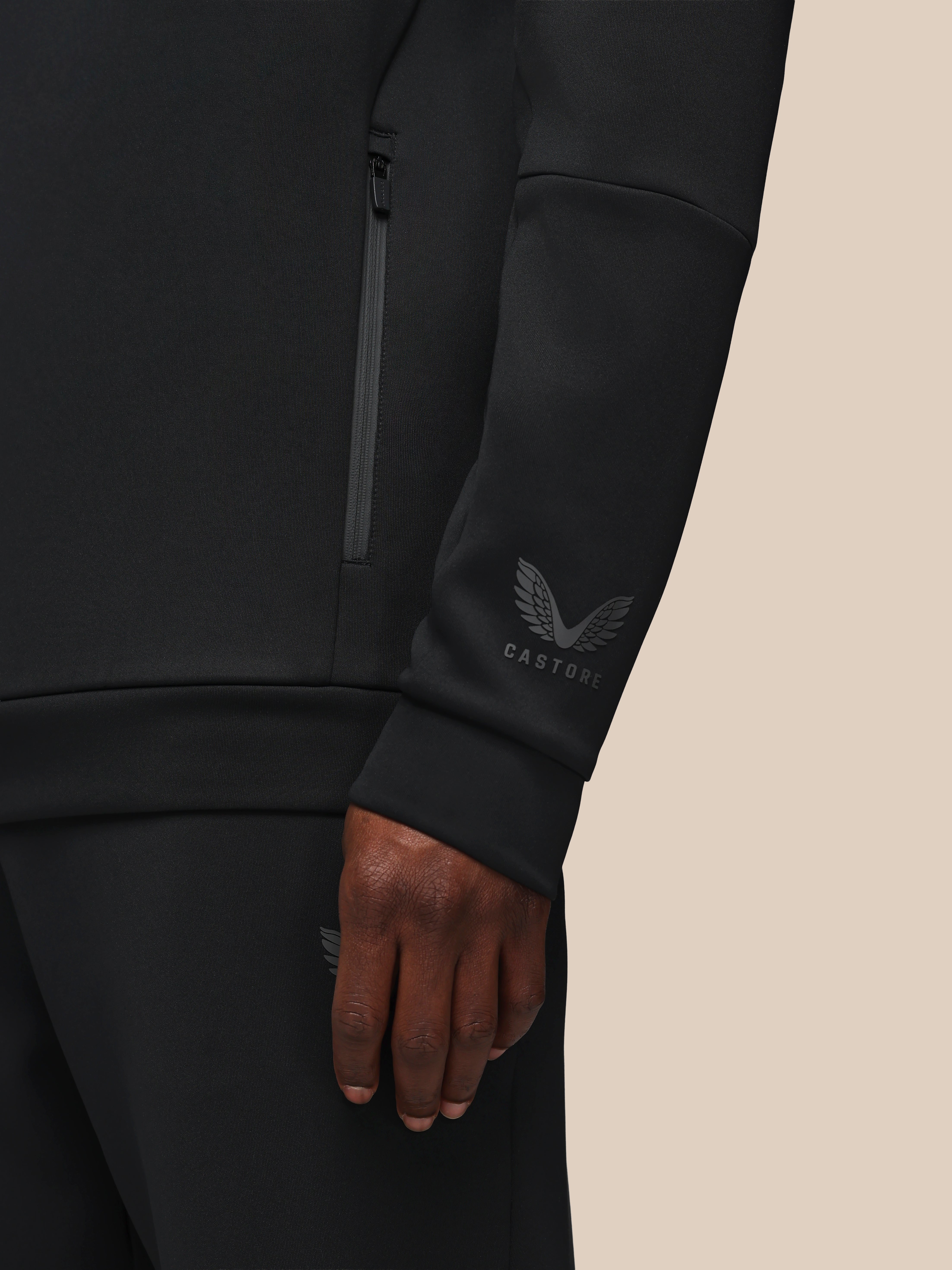 Black athletic jacket with brand logo on sleeve against a beige background