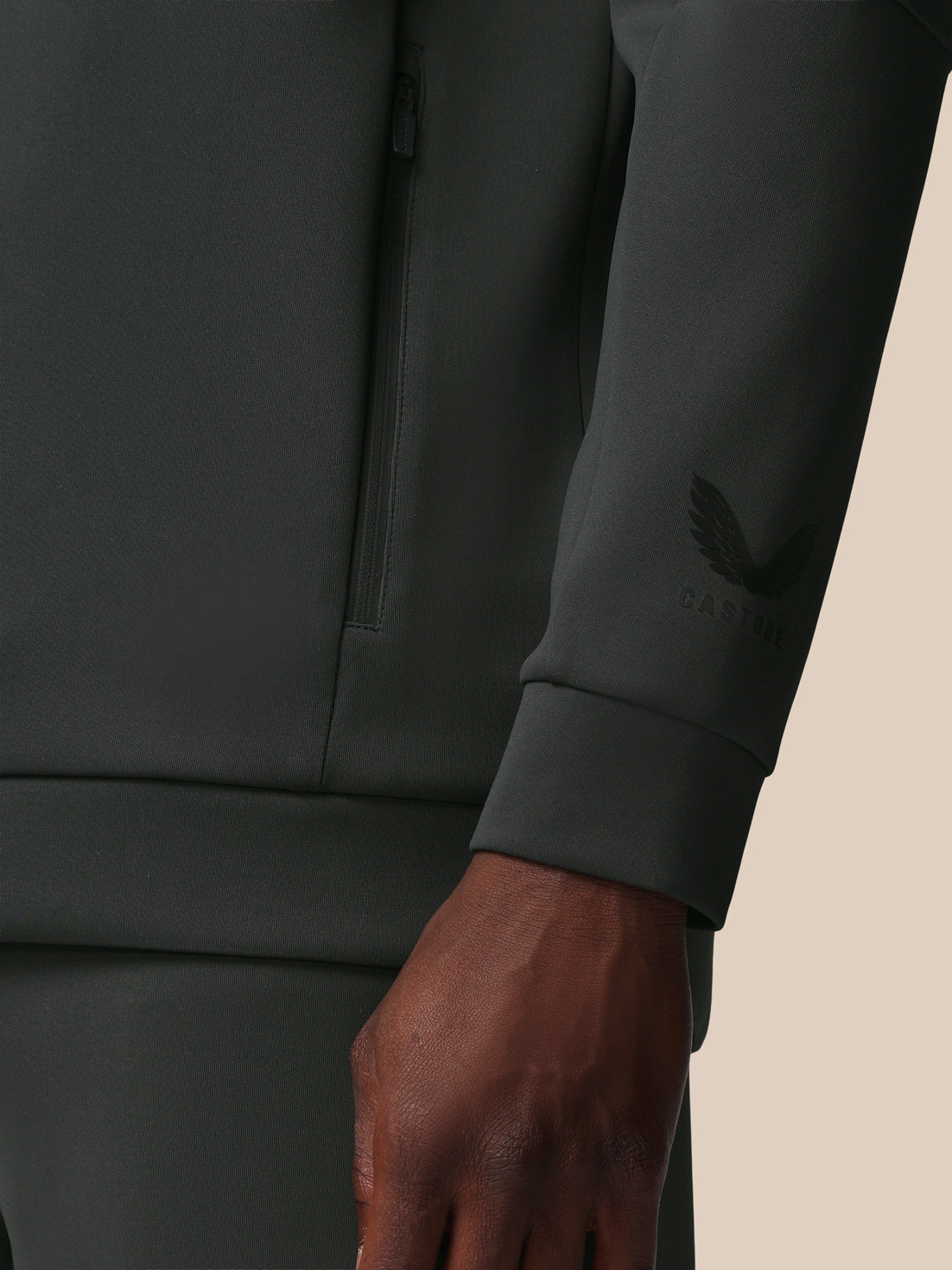 Close-up of a dark gray sweatshirt with a brand logo on the sleeve against a beige background