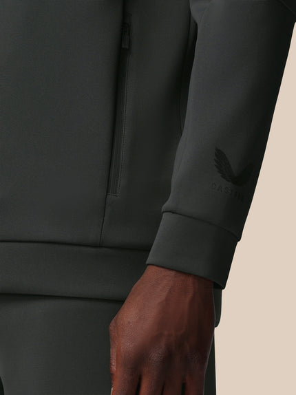Close-up of a dark gray sweatshirt with a brand logo on the sleeve against a beige background