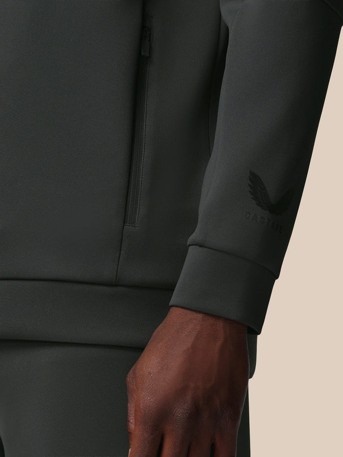 Close-up of a dark gray sweatshirt with a brand logo on the sleeve against a beige background