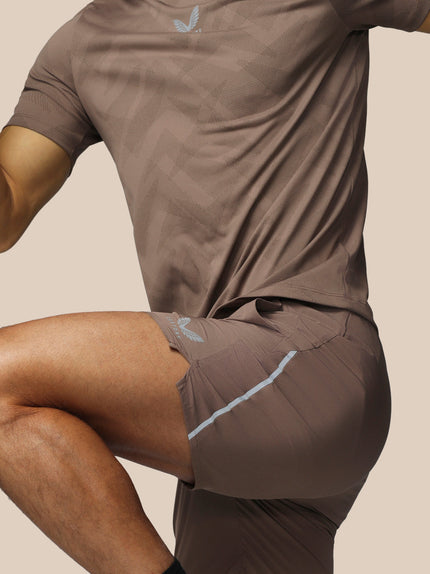 Person wearing brown athletic shorts and shirt with a logo on a beige background