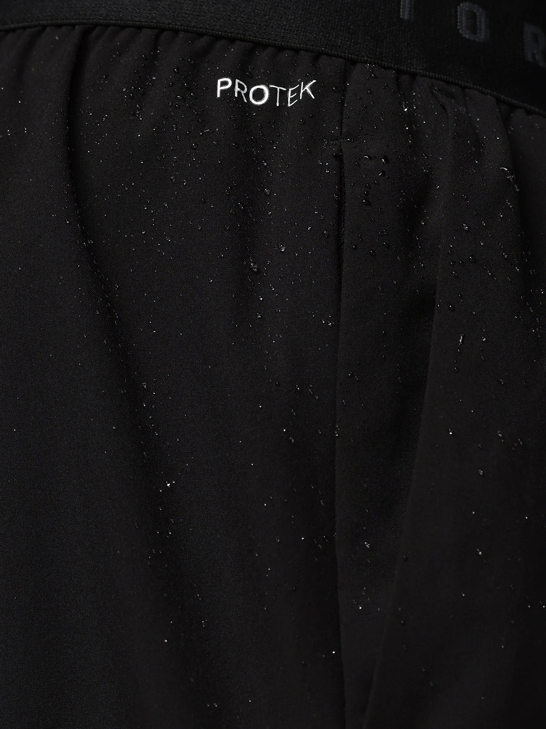 Close-up of a black jacket with 'PROTEK' branding on a dark background