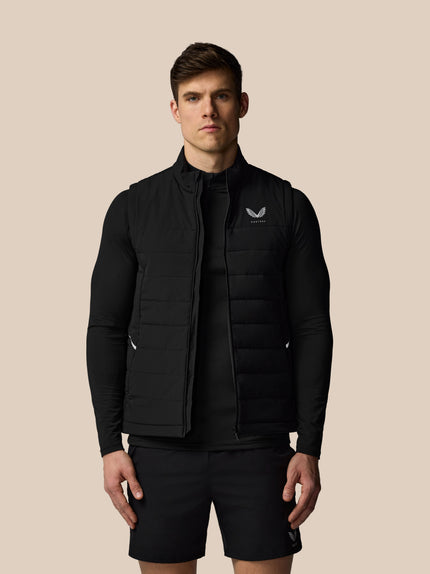 Man wearing a black puffer vest with a logo on a beige background