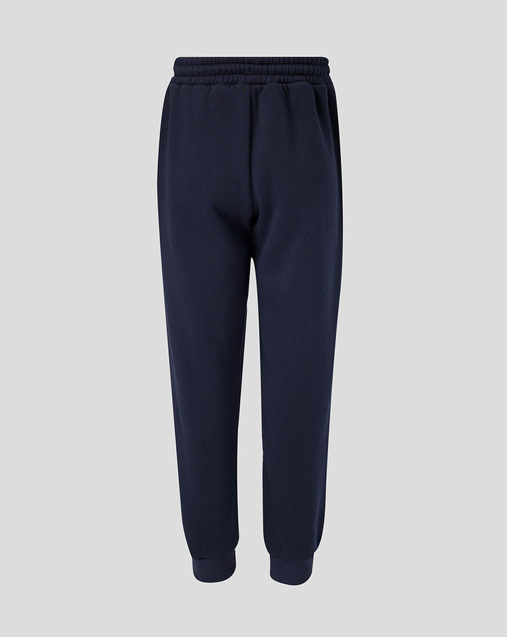 Full-length navy Travel Adapt fleece joggers with drawstring waist, crest on the left thigh and coral branding on the right.