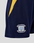 Close up of navy Preston North End home shorts with a yellow side stripe and club crest at the hem.