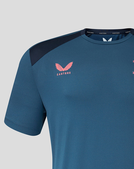 Close up of chest area showing pink crest logo on teal jersey with navy shoulder panel.