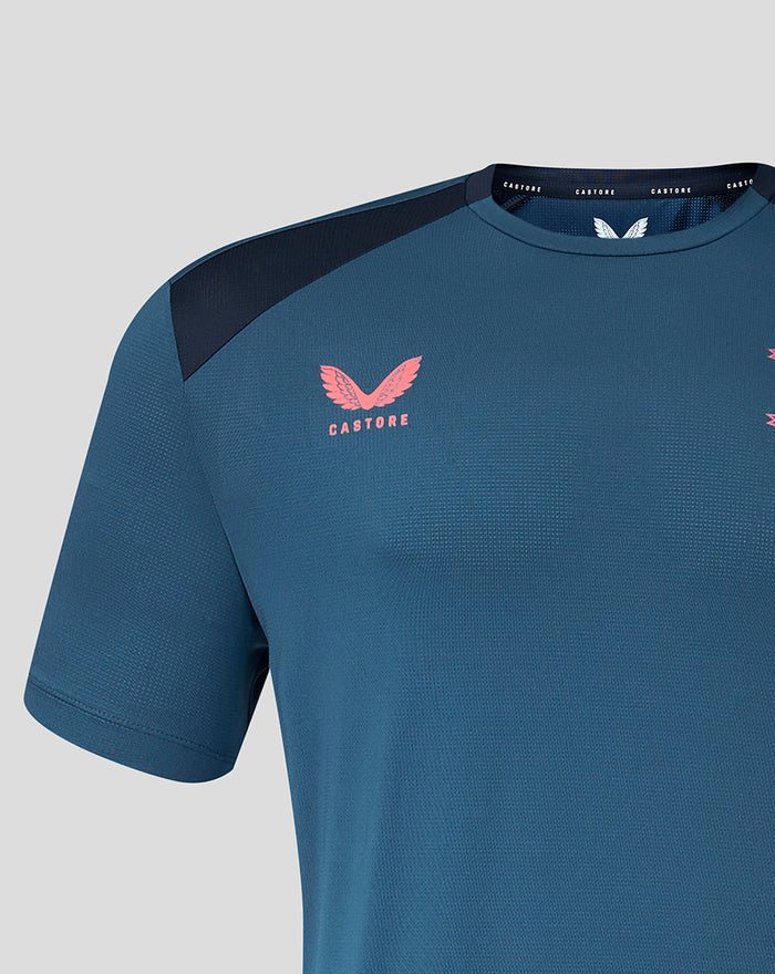 Close up of chest area showing pink crest logo on teal jersey with navy shoulder panel.