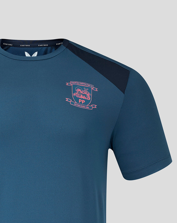 Left chest close up on teal training tee with pink crest badge and navy shoulder panel.