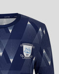 Close-up of the navy junior matchday shirt collar and shoulder showing the geometric pattern and partial club crest