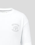Close-up of crest emblem on left chest of the white junior travel shirt.