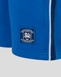 Back view of blue junior shorts featuring a crest patch and white side stripe