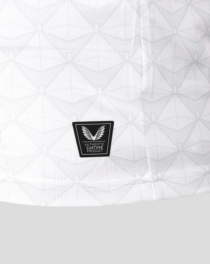 Lower front of the white junior shirt with a black Castore Authentic Product badge.