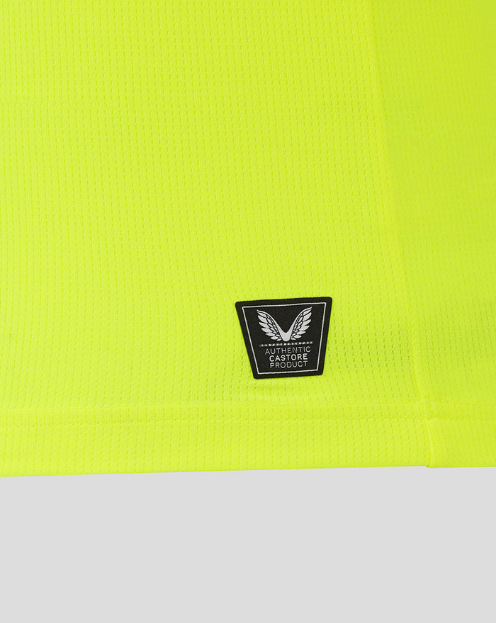 Close-up of neon lime fabric with a small black Authentic Castore Product badge near the hem.