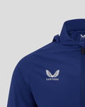 Close up of blue junior training packable hood shower jacket chest with the Castore logo and wings.