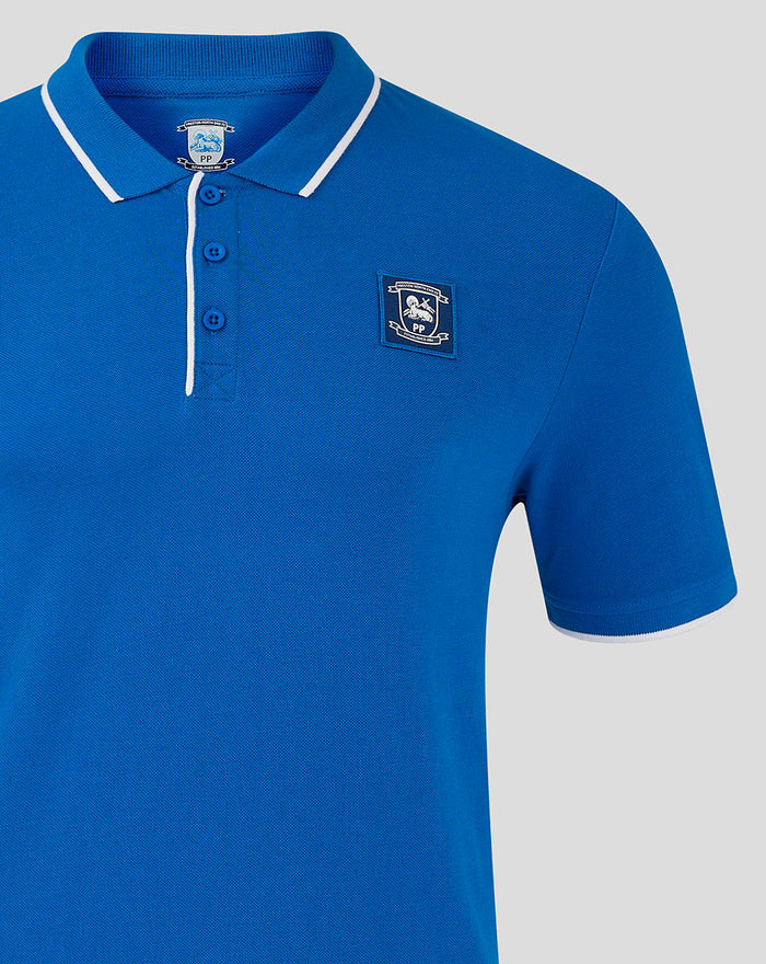 Blue polo shirt with crest badge on left chest and white piping along collar and placket