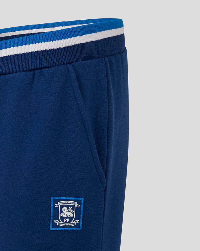 Navy jogger leg close-up showing striped rib cuff at ankle and a crest patch on the left thigh