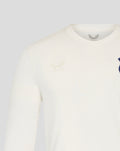 Close up of cream long sleeve shirt showing embossed Castore logo on left chest and blue Wembley crest on right chest.