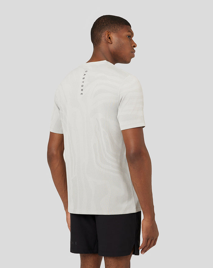 Back view of male model wearing light oyster Core Tech T shirt with subtle pattern and vertical Castore branding along the upper back.