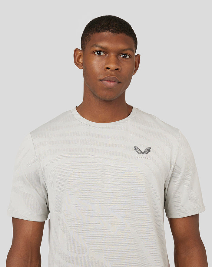 Male model wearing light oyster Core Tech T-Shirt with subtle pattern and small Castore logo on chest.