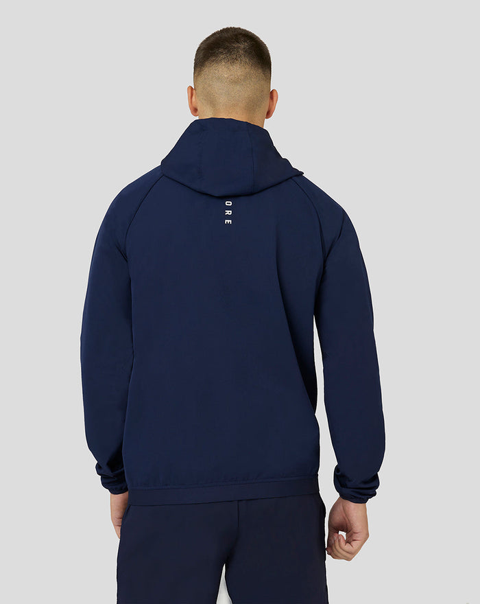 Back view of navy Apex Woven Hoodie on a model with hood down and vertical branding on the upper back