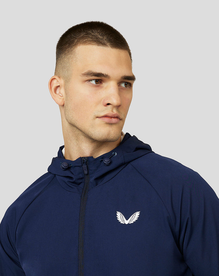 Three quarter view of navy Apex Woven Hoodie worn by a male model showing the front zipper and left chest logo
